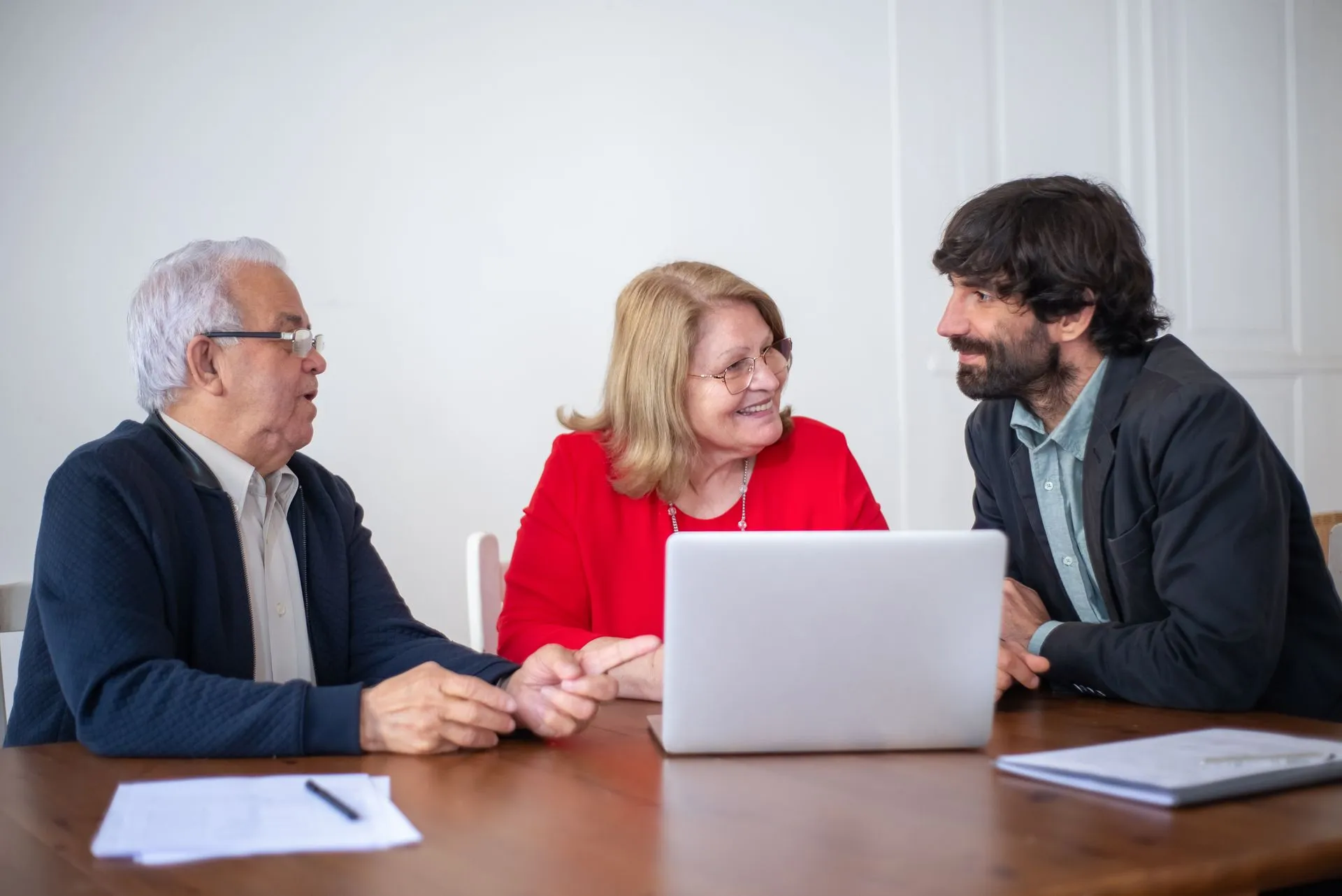 Um casal de idosos conversa com um profissional diante de um notebook, em uma mesa com papéis